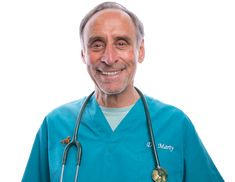 a man in scrubs and a stethoscope smiles at the camera while standing against a white background