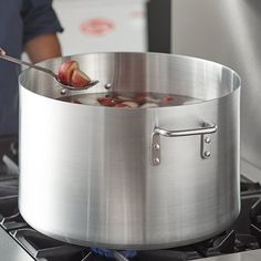 a person stirring food in a large pot on the stove with a ladle next to it