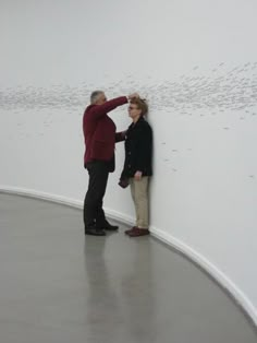 two people standing next to each other near a wall