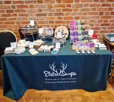 the table is covered with candles and other items for sale at an event in front of a brick wall