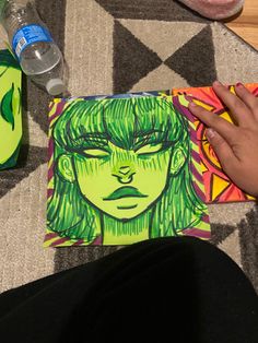 a person sitting on the floor next to a painting with green hair and an alien face