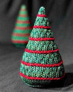 two small knitted christmas trees sitting on top of a bed next to each other