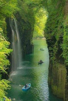 there is a waterfall in the middle of some trees and people are on small boats