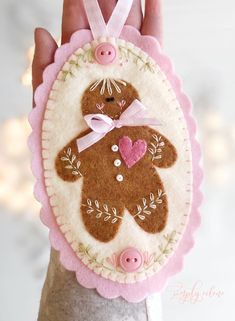 a hand holding a brown teddy bear ornament with pink buttons on it's side