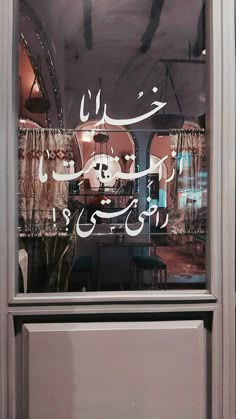 the reflection of two people in a shop's window with arabic writing on it