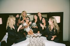 a group of women sitting on top of a bed holding wine glasses in their hands