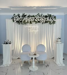 two white chairs sitting next to each other in front of a wall with flowers on it