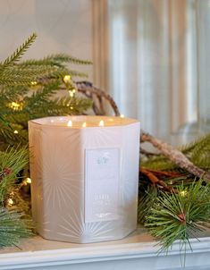 a white candle sitting on top of a mantle covered in pine needles and greenery