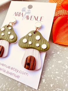 two wooden earrings with mushrooms on them sitting next to an orange ribbon