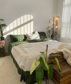 a bedroom with white walls, green bedding and potted plants in the corner