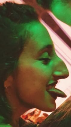 a woman with her tongue out and green light shining on her face behind her head