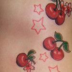 a woman's stomach with tattoos on it and some cherries attached to the side