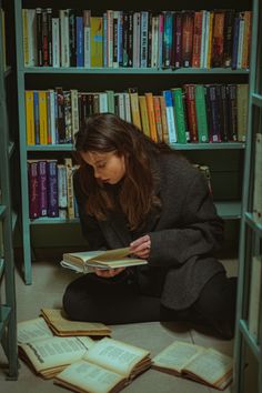 a woman sitting on the floor reading a book in front of a bookshelf