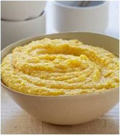 a white bowl filled with yellow food on top of a table next to two rolls