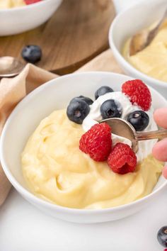 a person scooping berries into a bowl of oatmeal with yogurt and raspberries