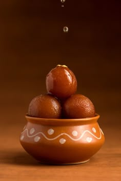 a brown bowl filled with oranges on top of a wooden table next to a drop of water