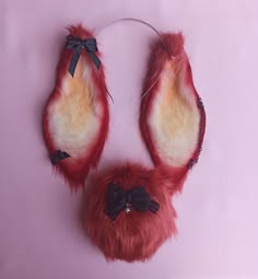 a pair of red furry mittens with bows and beads hanging on a pink wall