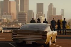 several people standing on top of a parking lot next to a car in front of a cityscape