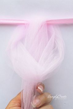 a hand holding a pink ribbon in front of a white background