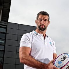 a man holding a rugby ball in his right hand and wearing a white polo shirt