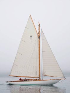 a small sailboat with white sails in the ocean on a foggy day,