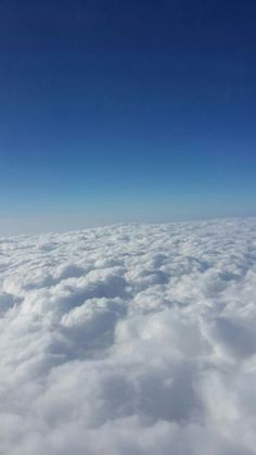 the view from an airplane looking down on some clouds and blue sky in the distance