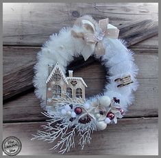 a white wreath with a house on it and decorations around the wreath is sitting on a wooden surface