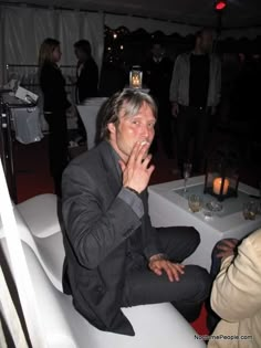 a man sitting on top of a white chair next to a table covered in candles