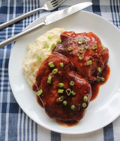 two meatballs covered in gravy and green onions on a plate with mashed potatoes