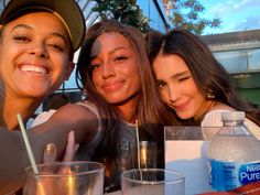 three girls are posing for the camera at a table with drinks and water in front of them