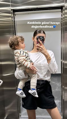 a woman taking a selfie with her child in front of an elevator stall door