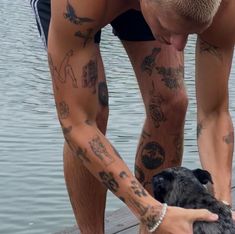 a man with tattoos on his arm petting a small black dog by the water