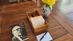 a desk with a pen, notepad and flower in a vase on the floor