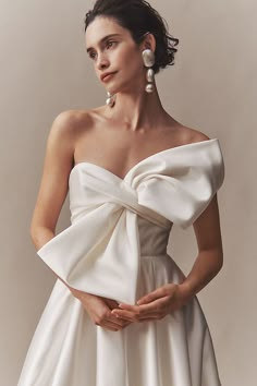 a woman in a white dress with her hands on her hips, wearing earrings and pearls