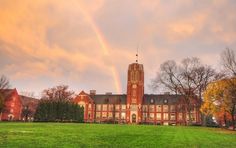 a large building with a rainbow in the sky above it on a green field next to trees