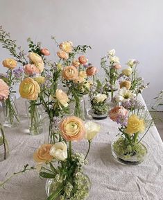 several vases filled with different types of flowers on a white tablecloth covered table