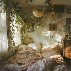 an unmade bed with plants hanging from the ceiling