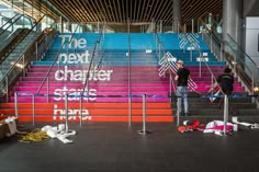 two people standing at the bottom of an escalator with colorful steps painted on it