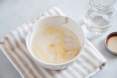 a white bowl filled with yellow liquid next to a glass of water and a spoon