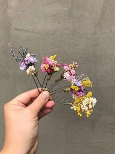 a person holding flowers in their hand on a gray background with concrete wall behind them