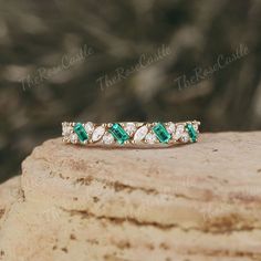 an emerald and diamond band ring sitting on top of a rock