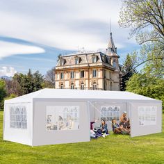 two people sitting in front of a large white tent with windows on the grass outside