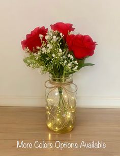 a glass jar filled with red roses and baby's breath on top of a wooden table