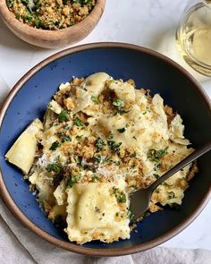 a bowl filled with pasta and cheese next to a glass of wine on a table