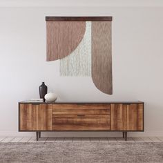 a sideboard with a vase on it in front of a wall hanging from the ceiling