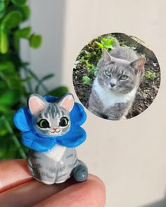 a small cat figurine with a blue flower on it's head is shown in front of a green plant