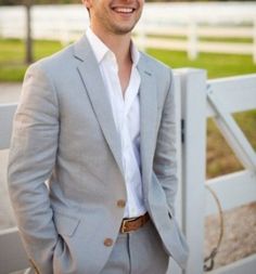 a man in a gray suit standing next to a white fence