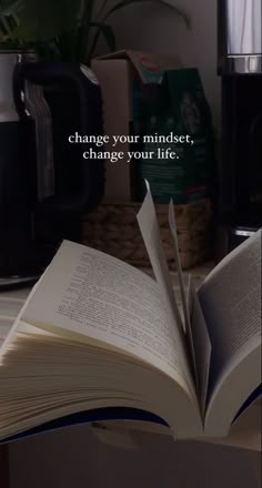 an open book sitting on top of a table next to a cup and coffee pot