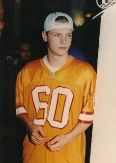 a young man standing next to a tall pole wearing an orange jersey with the number 50 on it