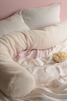 a bed with pillows and a bowl of popcorn sitting on top of it next to a pink wall